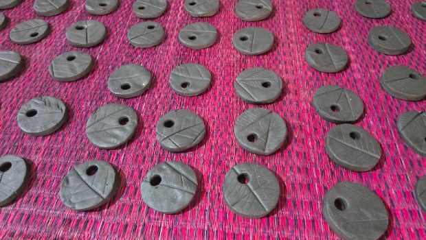 Dozens of round clay medals with hand-pressed leaf-vein patterns, laid out to dry on a red woven mat